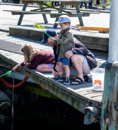 En pige og en dreng fisker efter krabber ved en mole. En far sidder på hug med dem.
