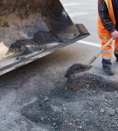 Mand i arbejdstøj skovler materiale til at lappe hul i vejen