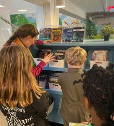 Børn på bibliotek med en bibliotekar, der leder efter bøger til dem.