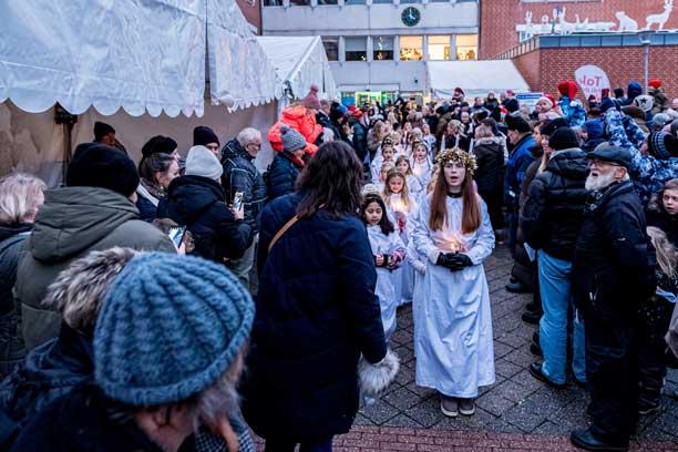 En ung luciabrud går syngende i front af et lucia-optog igennem en større menneskemængde