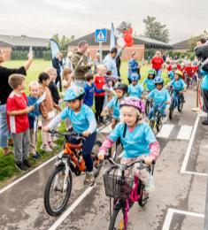 En masse små cyklister kører på en ny cykelbane, i baggrunden andre børn, der står og hepper.