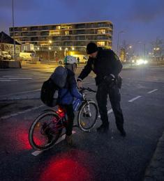 En politibetjent står foran et barn, der har standset sin cykel midt på cykelstien.