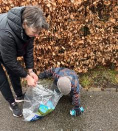 Et barn i flyverdragt samler en dåse op, mens en kvinde holder en klar plastikpose åben for barnet ved at bøje sig ned.