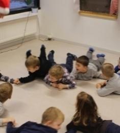 Børn ligger i en cirkel på gulvet og holder hinanden i hænderne.
