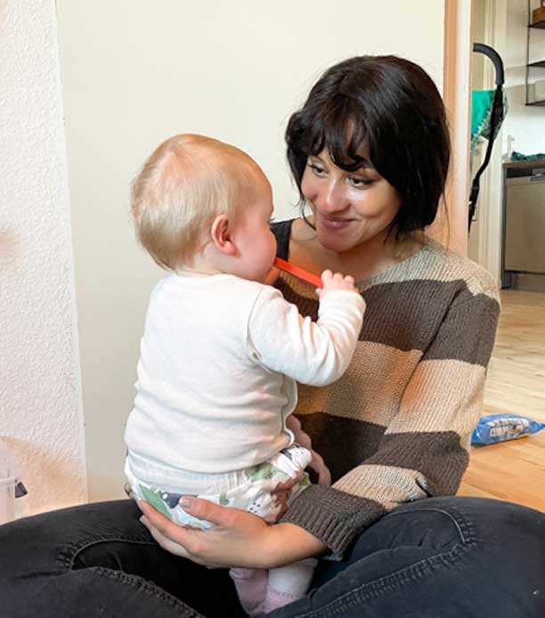 Yngre kvinde sidder i skrædderstilling på gulvet og har øjenkontakt med et barn, der sidder i hendes arme.
