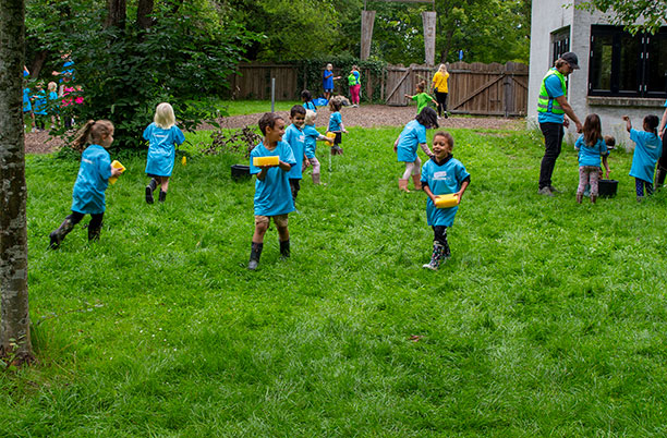 En gruppe af børn løber med gule svampe mellem spande i den ene ende af en bane og hen til en spand i den anden ende.