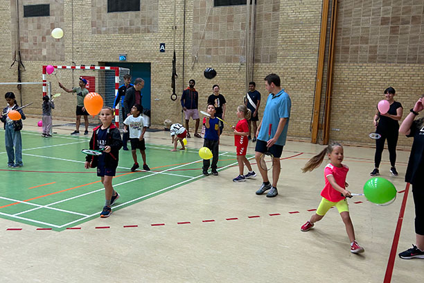 En masse børn i en stor idrætshal spiller ballon-badminton
