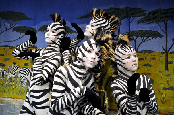 En gruppe børn er klædt ud i zebrakostumer og med ansigtsmaling. Bag dem et savannebillede