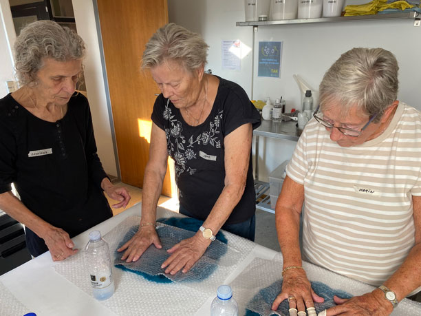 Tre ældre kvinder står med hver deres filtklump ved et bord.